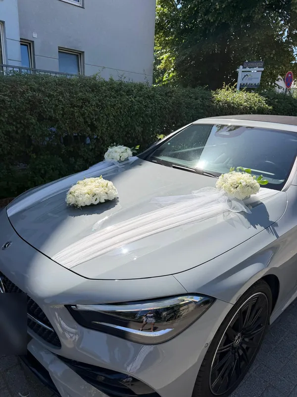 Grauer Mercedes mit weißen Rosengestecken und Tüll auf der Motorhaube
