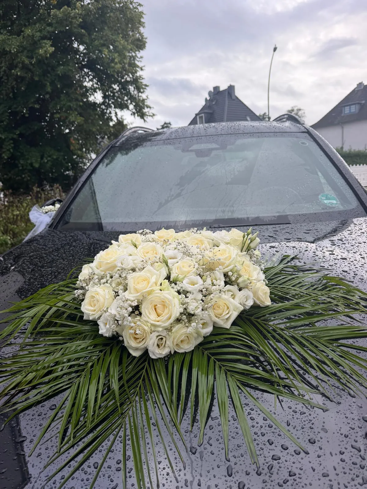 Schwarzer Brautwagen mit rundem weißen Rosenbogen auf Palmblättern