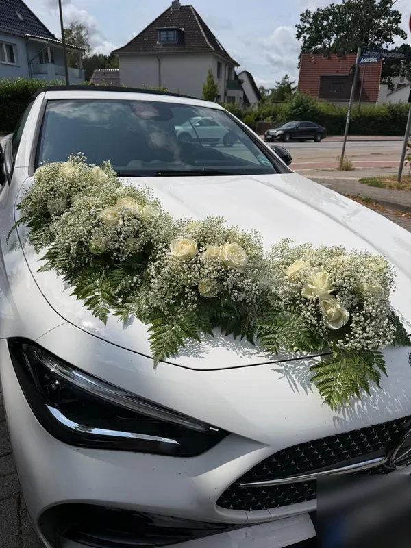 Weißer Mercedes mit Girlande aus weißen Rosen und Schleierkraut auf der Motorhaube