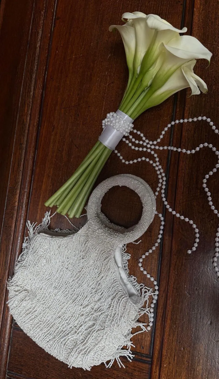Brautstrauß aus weißen Calla-Lilien mit Perlenband und Satinschleife auf dunklem Holz