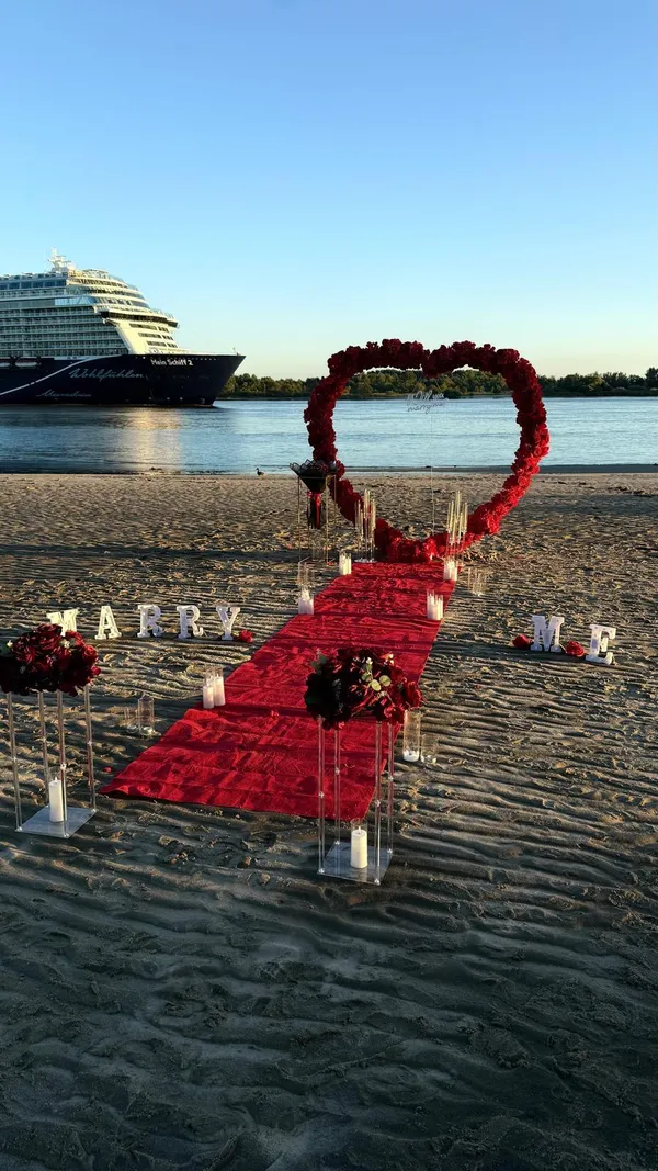 Heiratsantrag am Elbstrand bei Sonnenuntergang mit Herzbogen aus Blumen